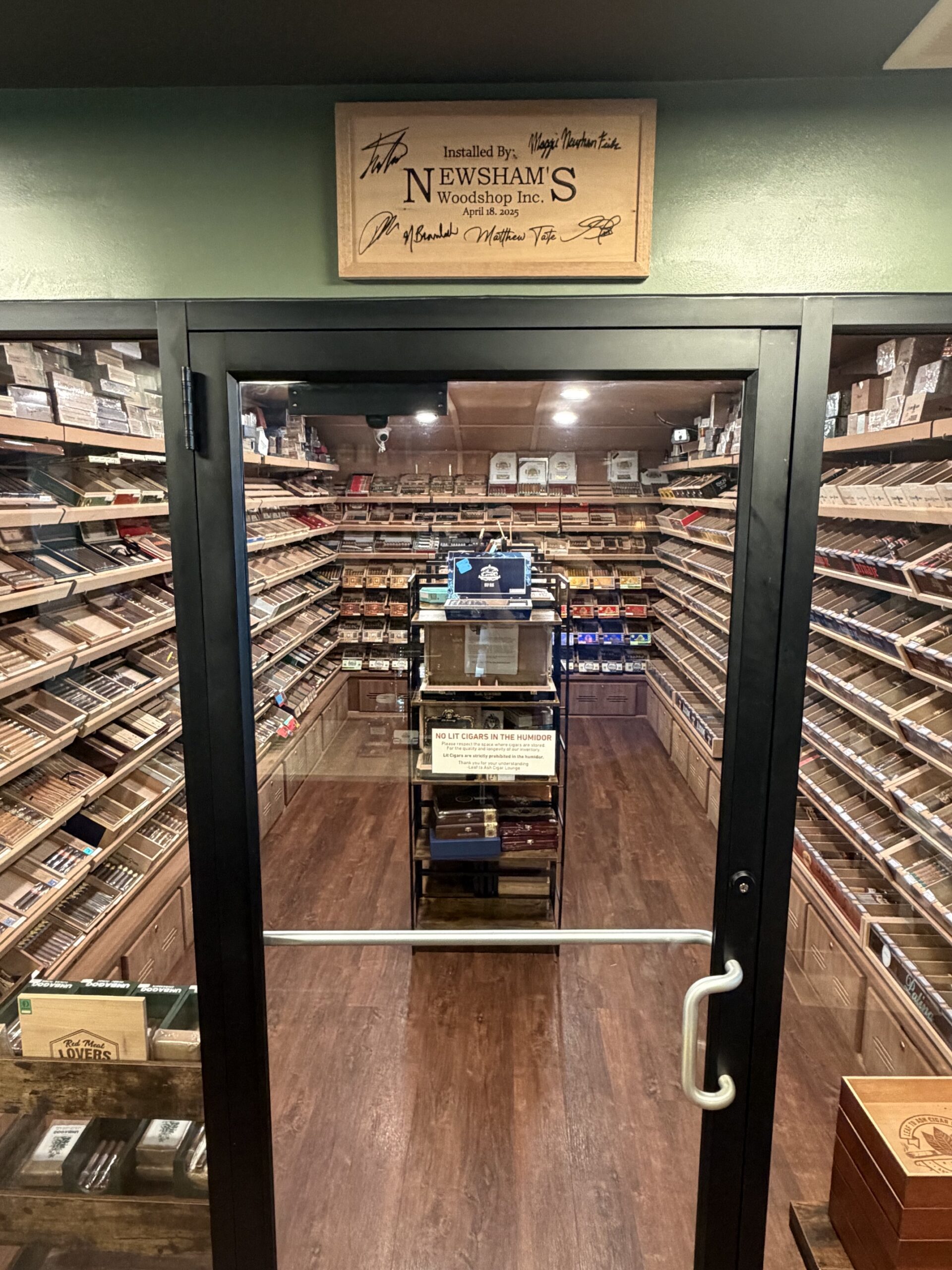 Leaf to Ash walk-in humidor entrance with Newsham’s Woodshop signed installation board above the door